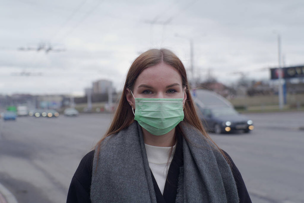 Beautiful young girl went outside in a medical mask. A girl in a medical mask looks at the camera. - Foto, afbeelding