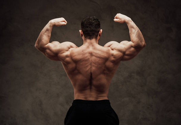 Hombre atlético posar hacia atrás mientras mira fuerte y mostrando sus músculos, aislado en el fondo gris
 - Foto, imagen