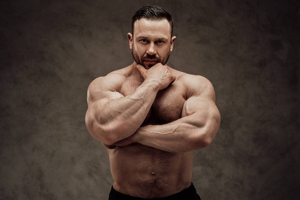 Shirtless adulto bodybuilder maschile posa, cercando premuroso e interessato a uno studio buio
 - Foto, immagini