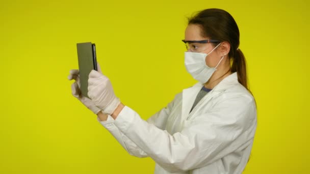 Žena v lékařském kabátě, ochranná maska používá rozšířenou realitu přes tablet - Záběry, video