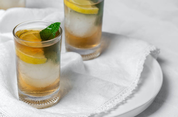 Refreshing glasses of tea with ice, mint and lemon wedges on white table - Φωτογραφία, εικόνα