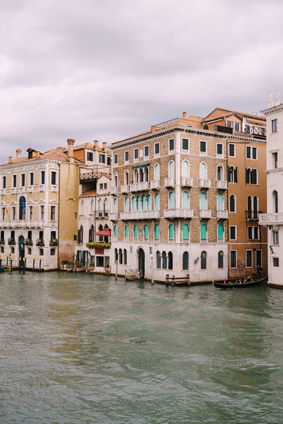 観光客とゴンドラはヴェネツィア、イタリアの水の上に立ってヴェネツィアの家のファサードの中にグランド運河に沿って航海しています. - 写真・画像