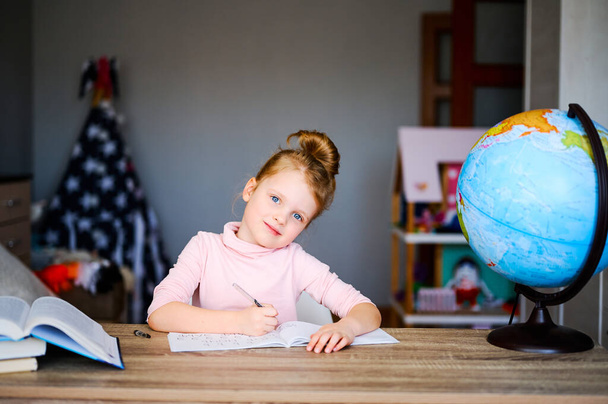 Назад в школу. Ребенок делает домашнее задание, сидит на столе, читает книги возле глобуса. Концепция дистанционного образования
 - Фото, изображение