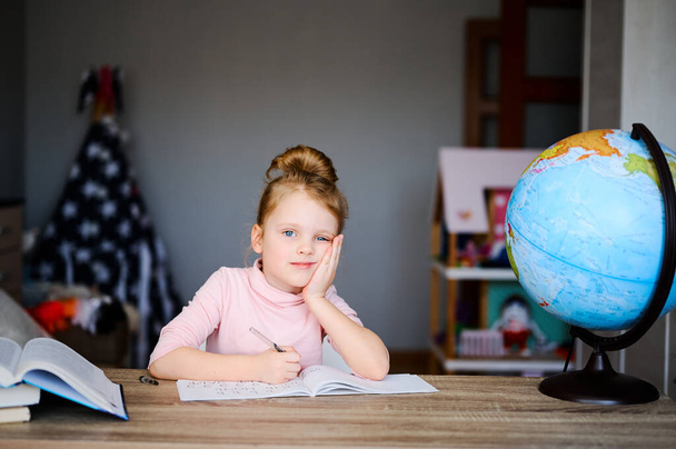 Назад в школу. Ребенок делает домашнее задание, сидит на столе, читает книги возле глобуса. Концепция дистанционного образования
 - Фото, изображение