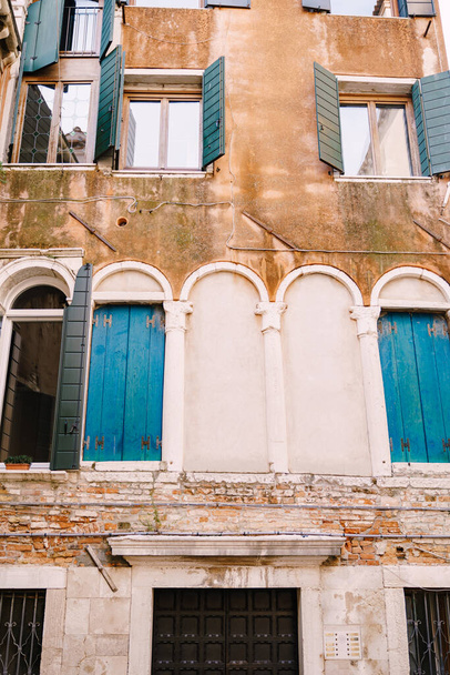Будівництво фасадів у Венеції, Італія. Фасад п'ятиповерхової будівлі з класичними венеціанськими арочними вікнами з дерев'яними віконцями. Стіни є червоною цеглою і розфарбовані персиковим кольором..  - Фото, зображення