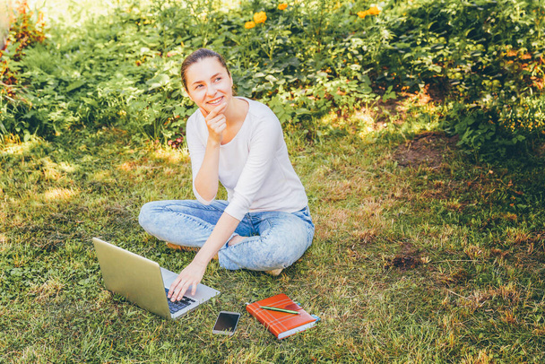 Mobile Office. Freelance business concept. Young woman sitting on green grass lawn in city park working on laptop pc computer. Lifestyle authentic candid student girl studying outdoors - Фото, зображення