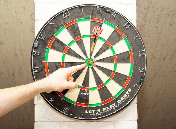 a man shows a dart stuck in the center of the darts, the result of skill and victory. - Photo, Image