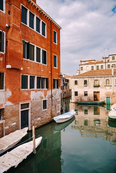 Σκάφη αγκυροβολημένα στους τοίχους ενός κτιρίου σε ένα κανάλι στη Βενετία της Ιταλίας. Κλασική Βενετική θέα στο δρόμο - ξύλινα παραθυρόφυλλα, πλίνθινα σπίτια, γέφυρες - Φωτογραφία, εικόνα