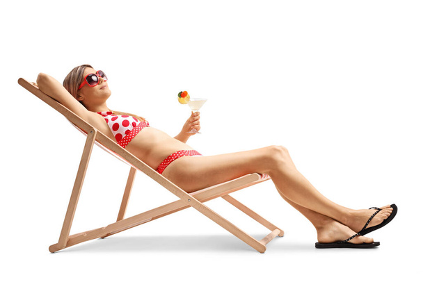 Young woman in bikini sunbathing on a lounge chair and holding a cocktail solated on white background - Fotografie, Obrázek