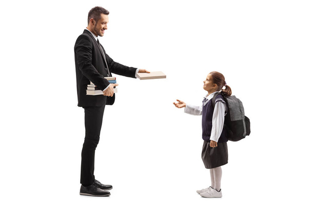 Full length profile shot of a man giving a book to a little girl in a school uniform isolated on white background - Foto, afbeelding