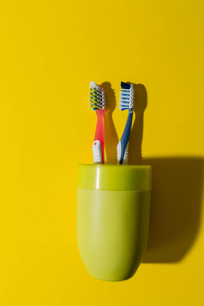 zwei Zahnbürsten in einem grünen Glas auf gelbem Hintergrund. rote und blaue Zahnbürsten. Schutz vor Karies. Zahnklinik. - Foto, Bild