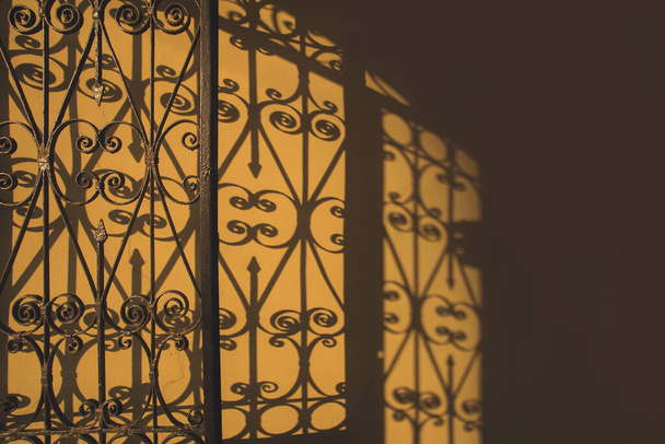 Żelazo kute ruszty ogrodzenie brama kontrast cień na ścianie w świetle poranka. Ciepłe żółte brązowe kolory. Zdjęcie z wolną przestrzenią do kopiowania tekstu. - Zdjęcie, obraz