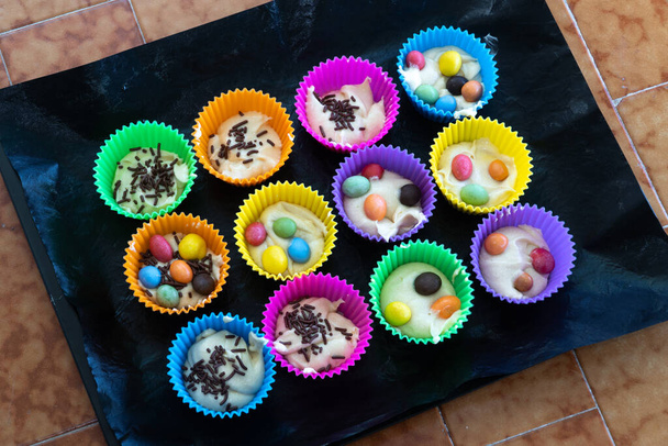 Köstliches Gebäck, das zu Hause zubereitet wird. Hausgemachte Cupcakes in bunten Silikonformen und mit farbigen Pralinen drinnen auf einem Backblech. Hausgemachte Kuchen für die Familie - Foto, Bild