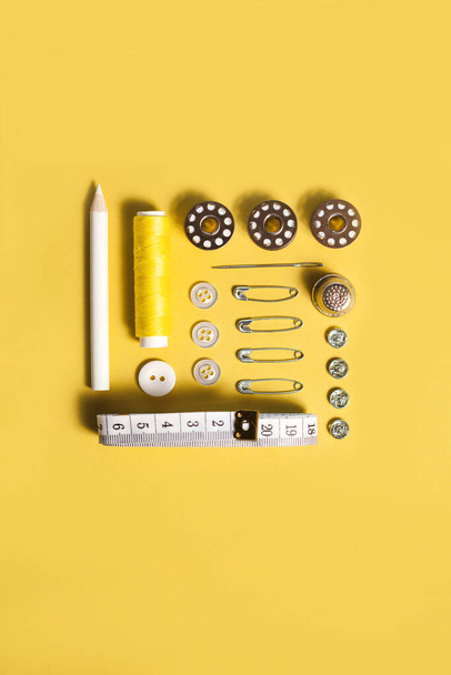 Sewing kit accessories and tools for needle work in yellow. Tape measure, pins, scissors, buttons, prewound bobbins, thimble, thread cutter flat lay. Knolling same color concept. - Fotó, kép