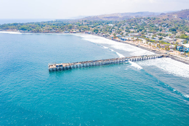 Вид с воздуха на прибрежную зону на пляже Ла-Либертад в Сальвадоре, где вы можете увидеть в целом его пирс и бирюзовую морскую воду
. - Фото, изображение