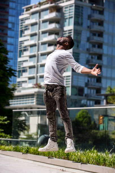 A Afro American black young man is levitating alone in a blurry background of a  downtown Vancouver in the midst of the quarantine, no mask, just fresh air, blue skies, urban blurry background, feeling of freedom and fresh air in a big port city - Fotó, kép