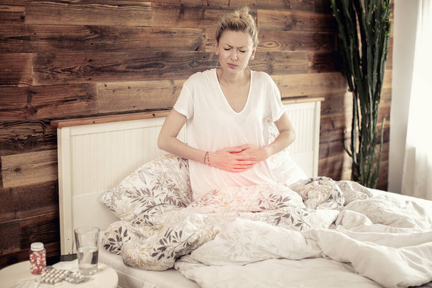 Kaukasische erwachsene Frau liegt mit Grippe, Erkältung und Fieber im Bett. Krankes Mädchen mit Bauchschmerzen. Quarantäne-Zeit. - Foto, Bild