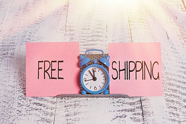Writing note showing Free Shipping. Business photo showcasing Freight Cargo Consignment Lading Payload Dispatch Cartage Mini blue alarm clock standing above buffer wire between two paper. - Photo, Image