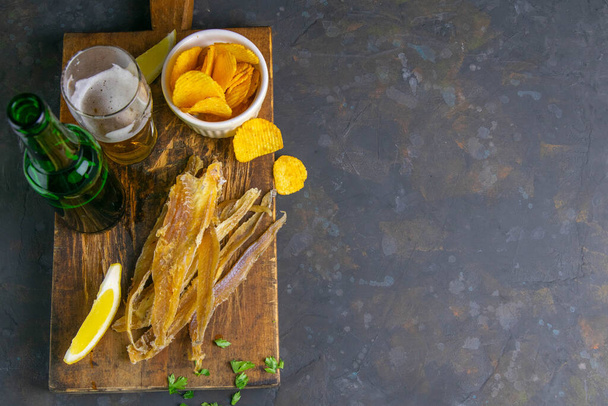 Filet de thon séché avec bière, citron et croustilles sur une planche de bois foncé. Snack sur le poisson avec de la bière. Top vues avec espace libre
. - Photo, image
