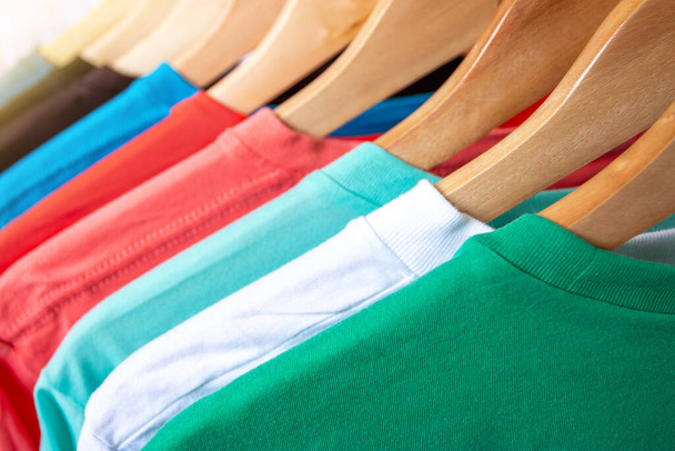 Fashion T-shirt op kledingrek - Close-up van felgekleurde kast op houten hangers in voorraadkast - Foto, afbeelding