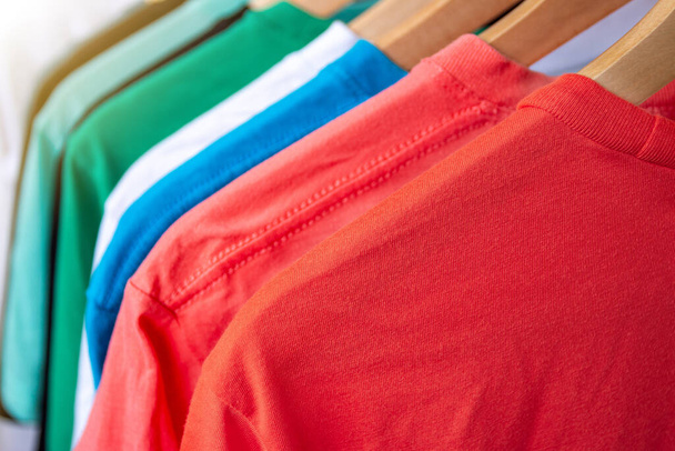 Moda T-shirt na stojaku na ubrania - zbliżenie jasne kolorowe szafy na drewniane wieszaki w szafie sklepu - Zdjęcie, obraz