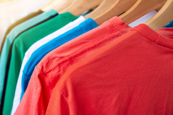Giysi rafındaki moda tişörtü - Dolaptaki ahşap askılarda parlak renkli dolabın kapatılması - Fotoğraf, Görsel