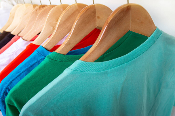 Fashion T-shirt on clothing rack - Closeup of bright colorful closet on wooden hangers in store closet - Photo, Image
