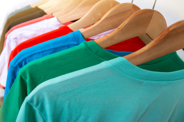 Módní tričko na věšáku na šaty - Detailní záběr pestrobarevné skříně na dřevěných ramínkách ve skříni skladu - Fotografie, Obrázek