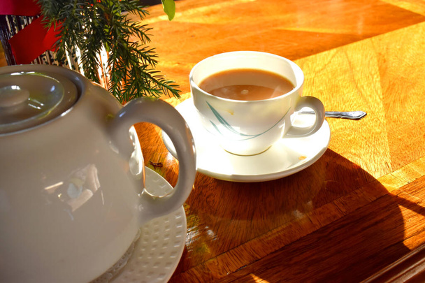 Uma xícara de chá quente com leite na caneca, colher de chá e panela, colocar em mesa de madeira e luz brilhante em afternonn ensolarado, chá inglês tradicional
. - Foto, Imagem