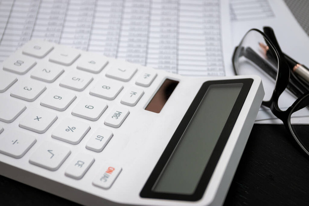 Οικονομικά έγγραφα και λευκά αριθμομηχανές σε μαύρα ξύλινα γραφεία - Φωτογραφία, εικόνα