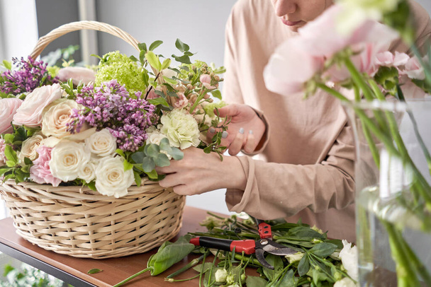 花屋のコンセプト。花屋の女性はウィッカーバスケットに花の配置を作成します。混合花の美しい花束。新鮮な束を。花配達. - 写真・画像