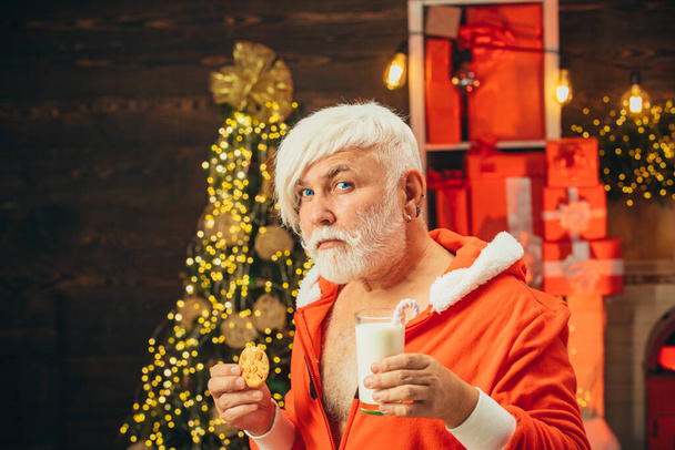 Merry Christmas and happy new year. Christmas cookies and milk. Santa Claus holding Christmas cookies and milk against Christmas tree background. - Foto, afbeelding