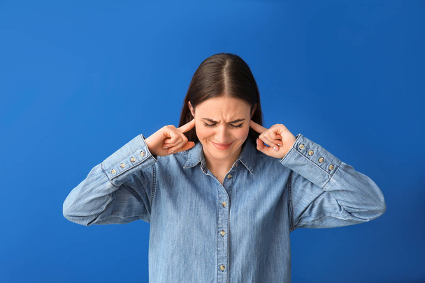 Junge Frau leidet unter lauten Geräuschen auf farbigem Hintergrund - Foto, Bild