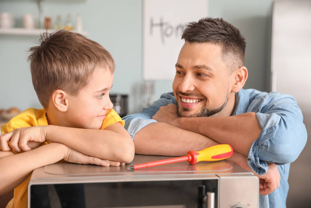 Kleiner Sohn hilft Vater bei Reparatur von Mikrowelle in Küche - Foto, Bild