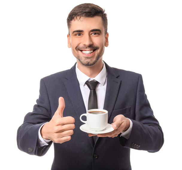 Jonge zakenman met kopje hete koffie tonen thumb-up op witte achtergrond - Foto, afbeelding