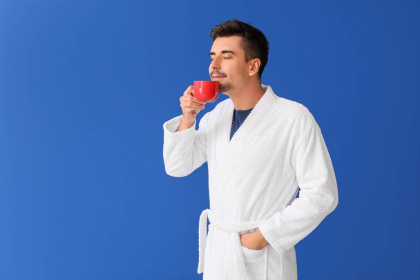 Mladý muž s šálkem horké kávy na barevném pozadí - Fotografie, Obrázek