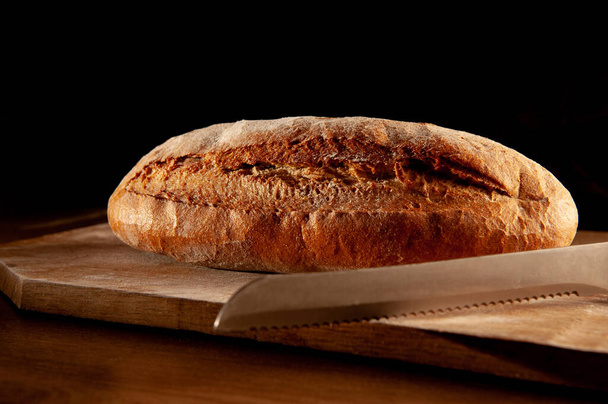 цілий запечений хліб на дерев'яній дошці на чорному фоні
 - Фото, зображення