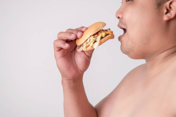 Ludzie z nadwagą jedzą hamburgery lub fast food. Śmieciowe jedzenie prowadzi do otyłości, ludzie mają tendencję do przejedzenia się. Izolowane białe tło. - Zdjęcie, obraz
