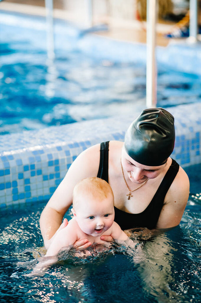 Młoda matka, instruktorka pływania i szczęśliwa dziewczynka w basenie. Uczy dziecko pływać. Ciesz się pierwszym dniem pływania w wodzie. Mama trzyma dziecko przygotowujące się do nurkowania. wykonywanie ćwiczeń - Zdjęcie, obraz