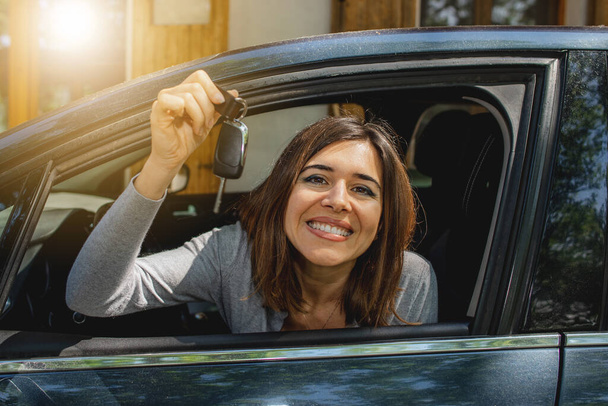 giovane donna felice in auto guardando fuori dal finestrino sorridente e mostrando la chiave della nuova auto. Nuova licenza. - Foto, immagini
