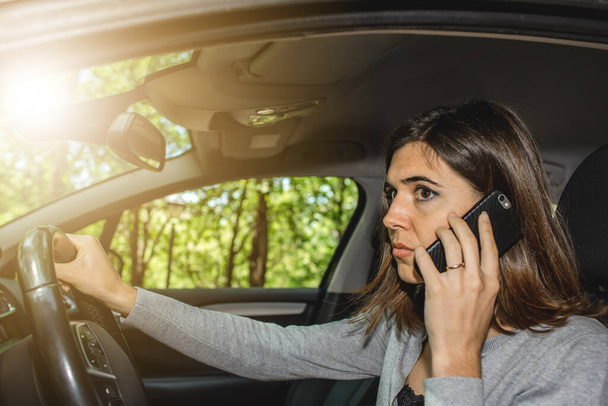 テキストメッセージと交通事故を引き起こす危険性のある携帯電話で話している間、若い女性が車を運転している肖像画。運転罪. - 写真・画像