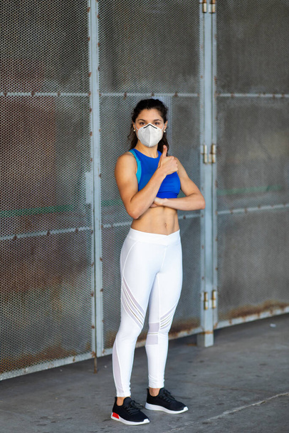 Jeune athlète féminine en forme avec un masque facial pour se protéger contre Covid-19. Portrait de sportive à l'extérieur. Succès de l'entraînement et mode de vie sain concept
. - Photo, image