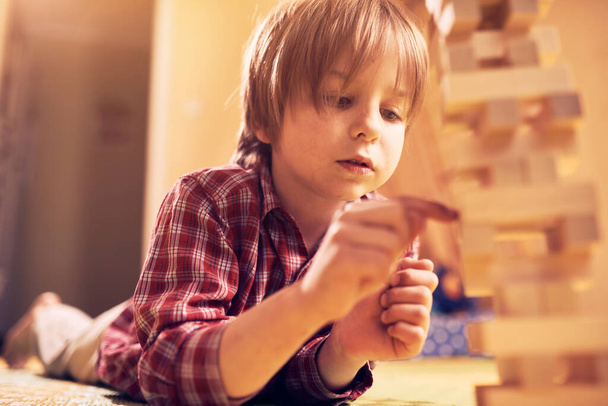 Preschool cute boy playing in a table game with wooden blocks at home. Players take turns removing one block at a time from a tower. Each block removed is then placed on top of the tower. - Fotografie, Obrázek