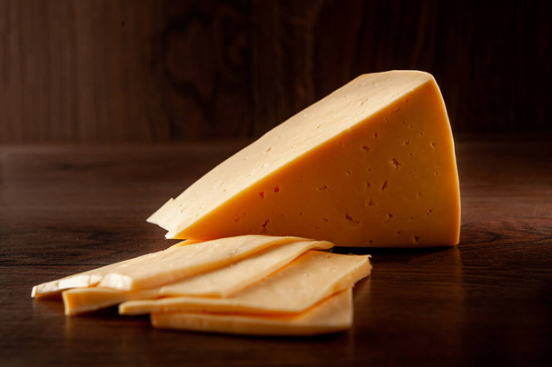 Cheese whole and pieces on a wooden background - Zdjęcie, obraz