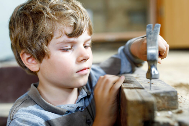 Boldog kisfiú segít a játékszerekkel az építkezésen. Vicces gyerek 7 éve szórakozik az új családi ház építésén. Gyerek körmök és kalapács segít apának felújítani a régi ház - Fotó, kép