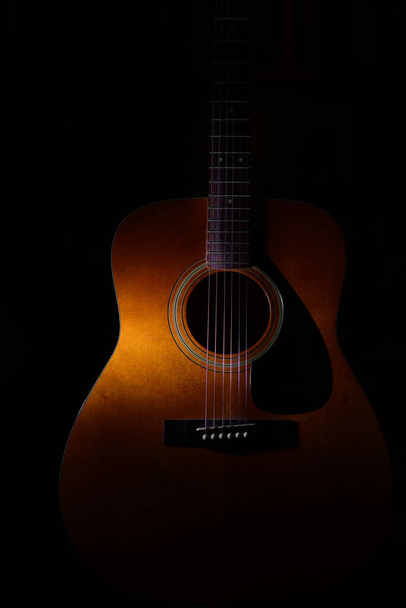 光と影の間の黒の背景のアコースティックギターの詳細 - 写真・画像