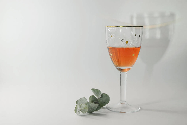 Vintage wine glass with rose wine and a branch of eucalyptus on a white background. On the wall is a reflection from a wine glass. Copy space. - Fotografie, Obrázek