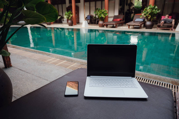White Laptop at the swimming pool and smartphone, workspace at a freelancer on vacation. - Photo, Image