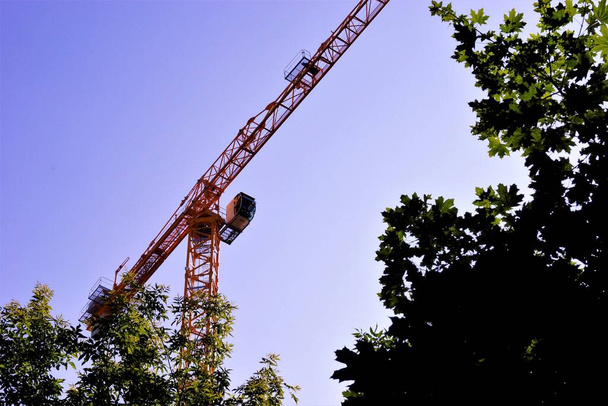 Turmdrehkrankonstruktion mit einem Pfeil auf dem Hintergrund des Himmels und der Bäume. Räumliche Beförderung von Gütern durch Hebemaschine, mit dem Einsatz von Haken- und Spannaufhängungen. - Foto, Bild
