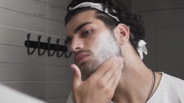 Joven chico guapo aplicando espuma de afeitar y mirando el espejo en el baño
 - Metraje, vídeo